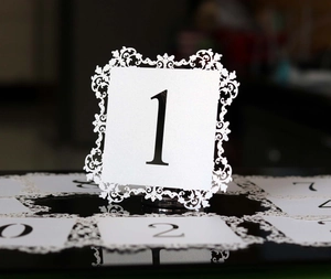 Detailed macro view of laser-cut lace wedding table number cards on glossy surface