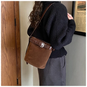 Brown suede bucket bag detail with dark leather trim and buckle strap accents