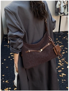 Detail of dark brown suede tote bag with golden buckle and elephant charm on grey suit