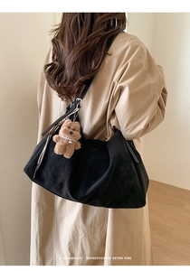 Detalle del bolso tote minimalista de ante negro con colgante de oso de peluche marrón