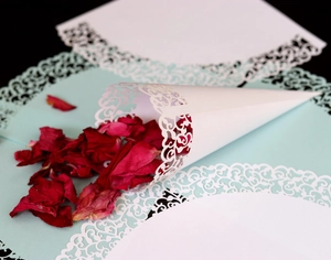 Macro shot of laser-cut white lace confetti cone with deep red dried rose petals