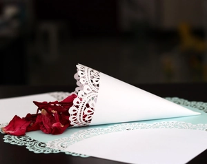 Close-up of white lace cutout wedding petal cone filled with red dried flowers