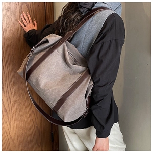 Detail of taupe canvas tote bag with brown leather straps worn on a person shoulder