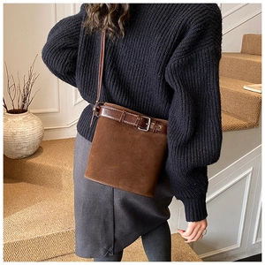 Detail view of coffee brown suede bucket bag with leather trim and metal buckle on stairs