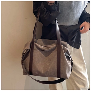 Close-up of taupe canvas tote bag with brown leather straps worn over the shoulder