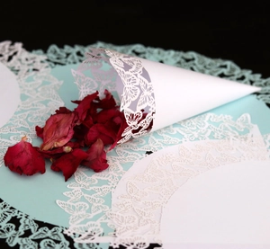 Macro detail of white laser-cut butterfly confetti cone with dried red flower petals