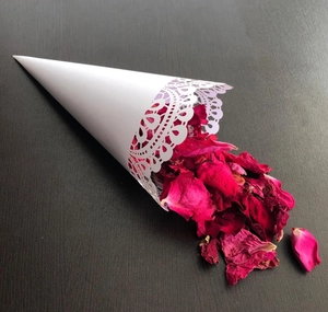 Macro view of white laser-cut lace cone for wedding petals with dried red rose details