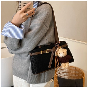 Detail shot of black leopard texture bucket bag with brown strap and plush bear charm