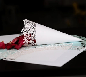 Macro detail of white laser-cut butterfly wedding cone filled with dried red rose petals