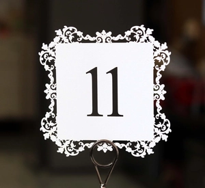 Detail of laser-cut white wedding table number 11 card with floral hollow pattern