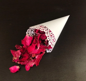 Detail of a white lace wedding paper cone filled with deep red dried rose petals