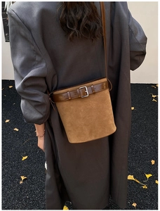 Brown suede bucket bag with leather strap and silver buckle on a grey autumn coat
