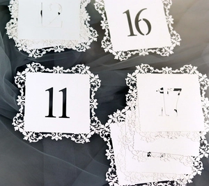 Detailed laser-cut white table number cards with ornate lace edges for wedding events