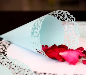 Macro view of light blue laser cut cone with lace edges and red rose petals for weddings
