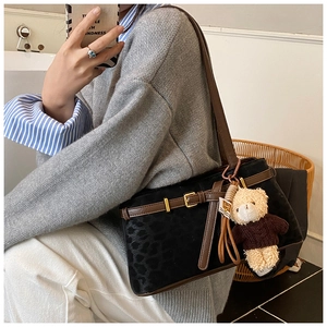 Detail of black suede leopard print bucket bag with brown leather strap and bear charm