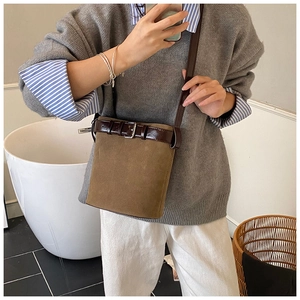 Close-up of brown suede bucket bag with dark leather trim worn as a crossbody bag