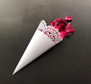 Close-up of white laser-cut lace confetti cone with dried red rose petals for wedding ceremony