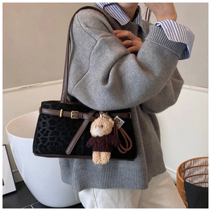 Detail of leopard print bucket bag with brown leather strap and plush bear charm accessory