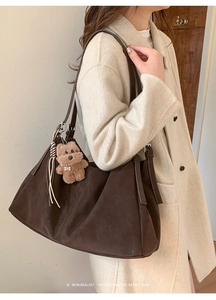Detalle del bolso tote de ante marrón oscuro con flecos y colgante de oso al hombro