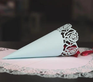 Détail du cône en papier bleu clair ajouré au laser avec pétales pour mariage chic