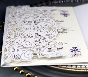 Close-up of laser-cut wedding invitation with white floral patterns and purple inner card