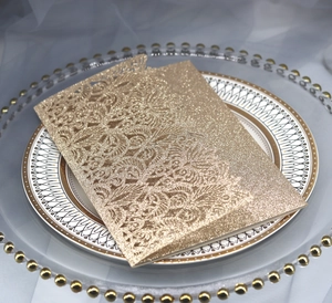 Champagne glitter laser cut invitation card with intricate floral patterns on a plate