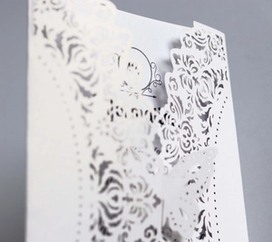 Macro shot of white laser-cut invitation card with butterfly and floral lace texture