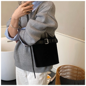 Detail view of black bucket bag with a belt buckle accent on a model's shoulder