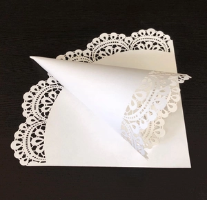 Detail of white lace paper cone and flat doily showing hollow patterns on wood background