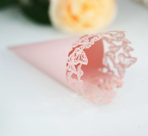 Detail of pink laser-cut wedding confetti cone with delicate butterfly hollow patterns