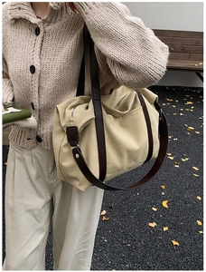 Detailed side view of a large canvas tote bag with brown leather straps worn outdoors
