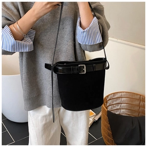 Side view of a black suede bucket bag with silver buckle worn by a model in casual attire