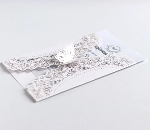 Detail of laser-cut white wedding invitation with intricate floral lace and butterfly clasp