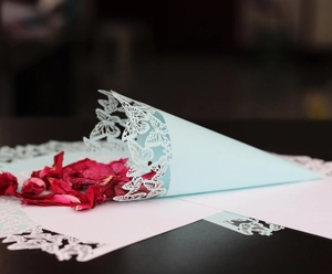 Detail of light blue laser-cut paper cone with butterfly pattern and red dried petals