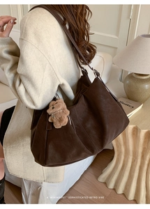 Detalle de un bolso tote grande de ante marrón con costuras y un colgante de osito
