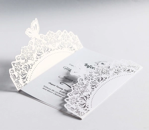 Macro shot of white laser-cut wedding invitation featuring butterfly lace and floral details