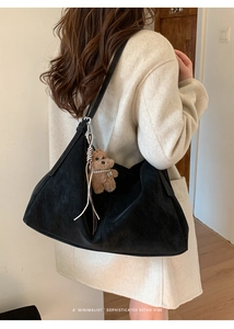 Detalle de un bolso tote de ante negro con un adorable colgante de oso de peluche suave