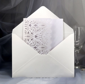Detailed laser-cut lace wedding invitation with white envelope on romantic background