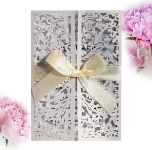 Close-up of laser-cut leaf patterns on ivory wedding invitation with silk ribbon bow