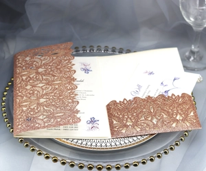 Detail of rose gold glitter laser cut invitation cover with elegant vine pattern on glass tray