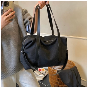 Detail of black canvas tote bag showing faux leather handles and adjustable shoulder strap