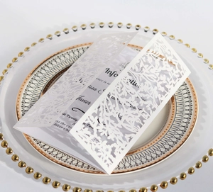Close-up of laser-cut wedding invitation card with elegant leaf patterns on a ceramic plate