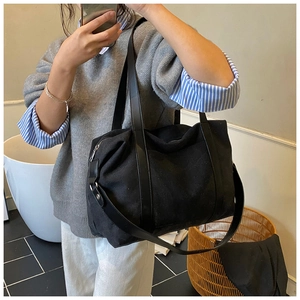Detail of a large black canvas tote bag showing reinforced leather straps and zipper closure