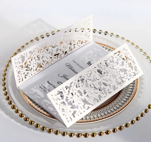 Detail of laser-cut wedding invitation with branch pattern on a formal dinner plate