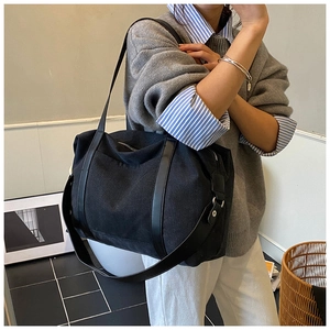 Close-up of black canvas tote bag with adjustable leather strap on model outfit