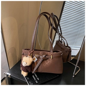 Detail of dark brown matte leather bucket bag featuring a decorative belt and bear charm