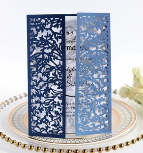 Intricate laser-cut navy wedding invitation with elegant leaf pattern on white ceramic plate