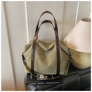 Detail of dark green canvas tote bag featuring premium brown leather handles and strap