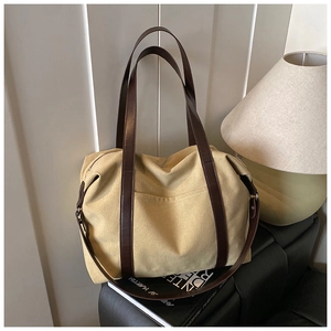 Detail of khaki canvas tote bag featuring brown leather handles and front patch pocket