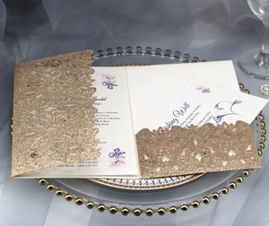 Detail of laser-cut rose gold glitter wedding invitation with floral insert on glass tray